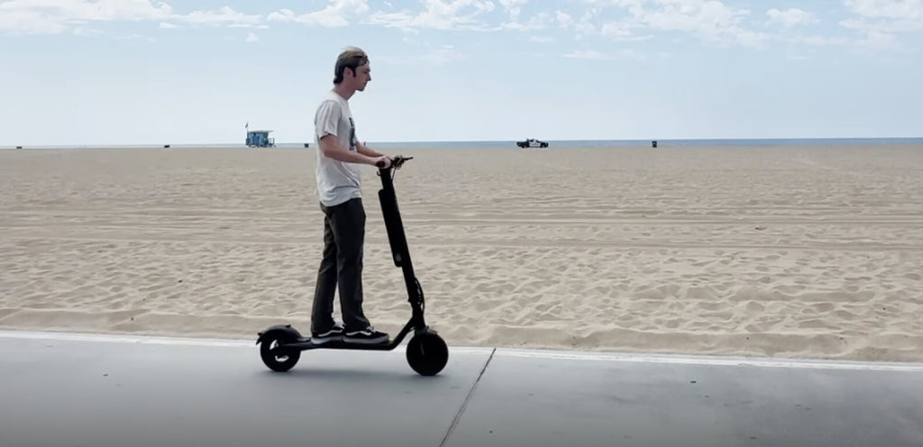Person riding a scooter on a sandy beach with a clear sky.