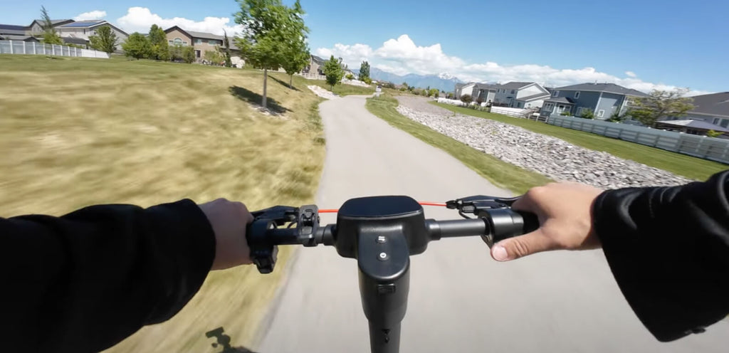 Person riding an electric scooter on a path with a suburban landscape in the background